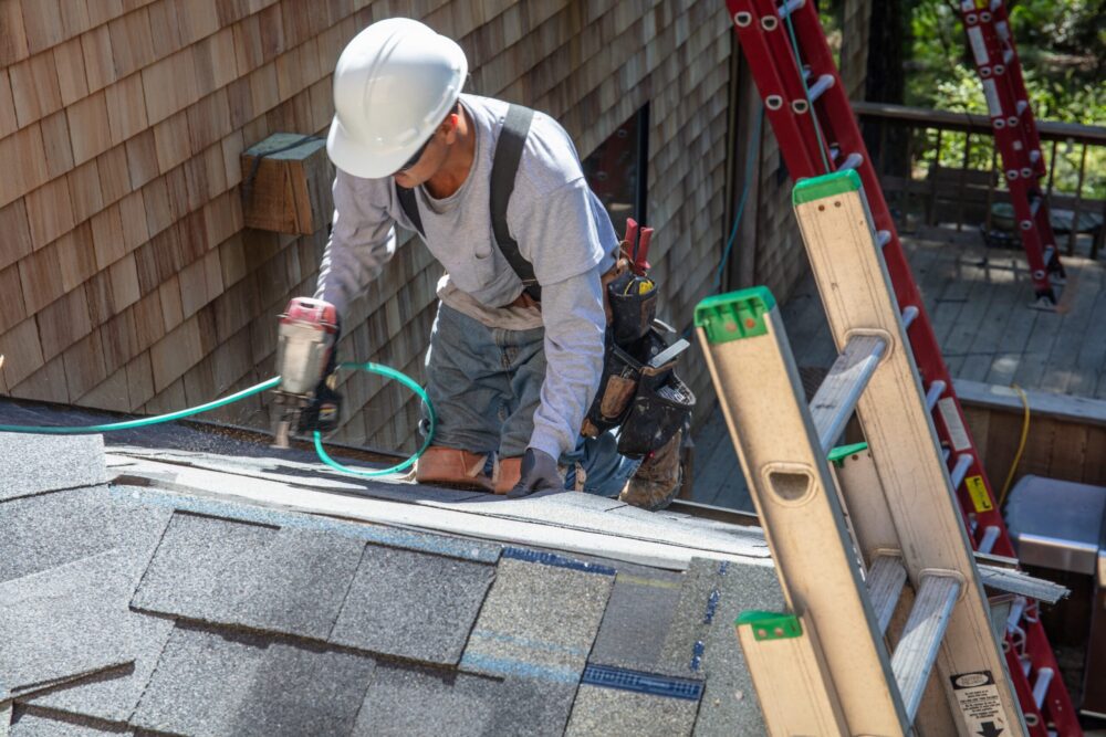 Roofer installing new roof with nail gun and shingles